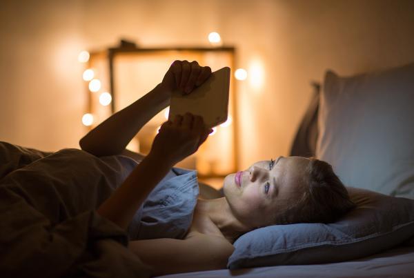 Young woman using her tablet computer in her bed late at night (color toned image; shallow DOF)